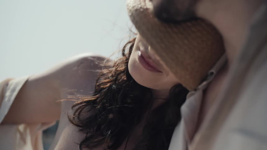 The video shows a closeup of a mans face with a woman resting her head on his shoulder the man is wearing sunglasses and a straw hat is partially visible