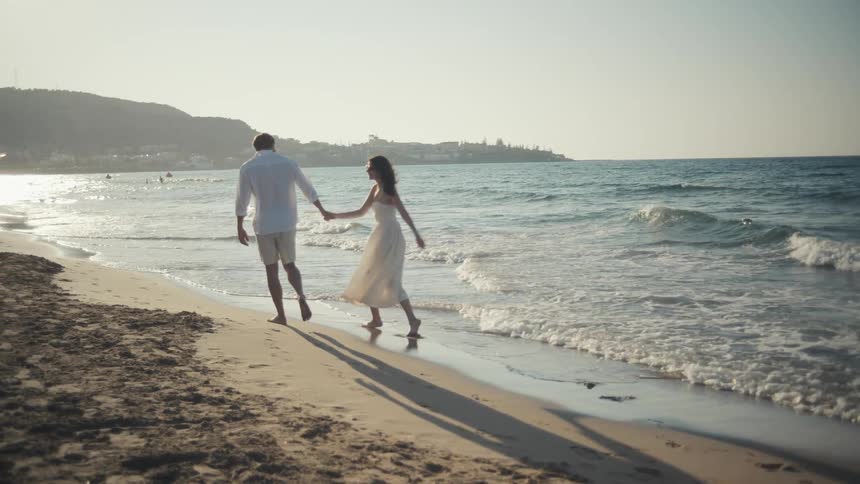 A couple walking down the beach holding hands and having fun at midday