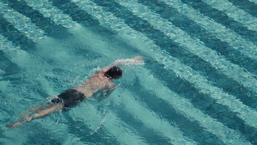A highangle shot captures a person swimming freestyle across a pool moving with a steady stroke with their back to the camera
