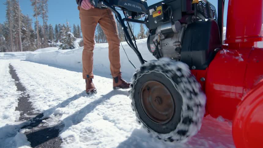 A man pushing a snow blower along the road clearing snow at midday