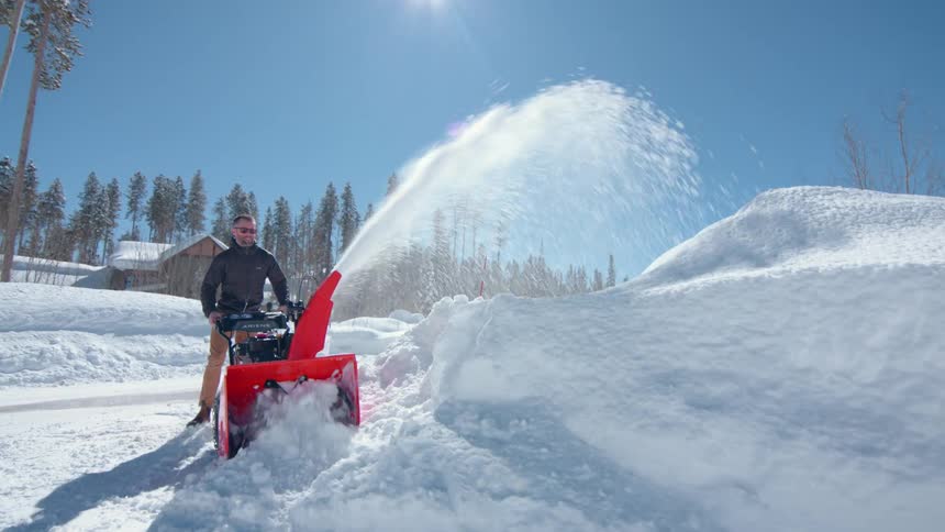 Man clears snow with snowblower on sunny winter day