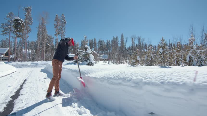 A man clearing snow from the road with a shovel at midday
