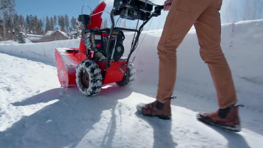 A man rolling an ariens snow blower on the road clearing snow during winter at midday