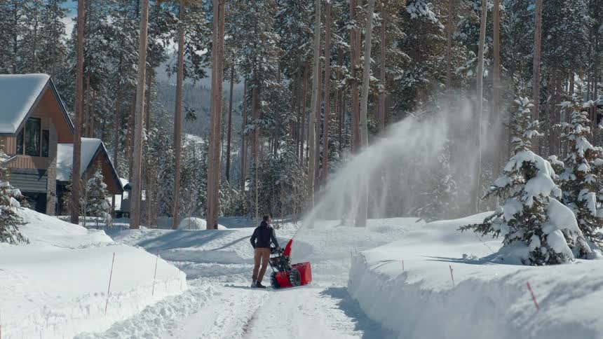 A man is snow blowing the driveway