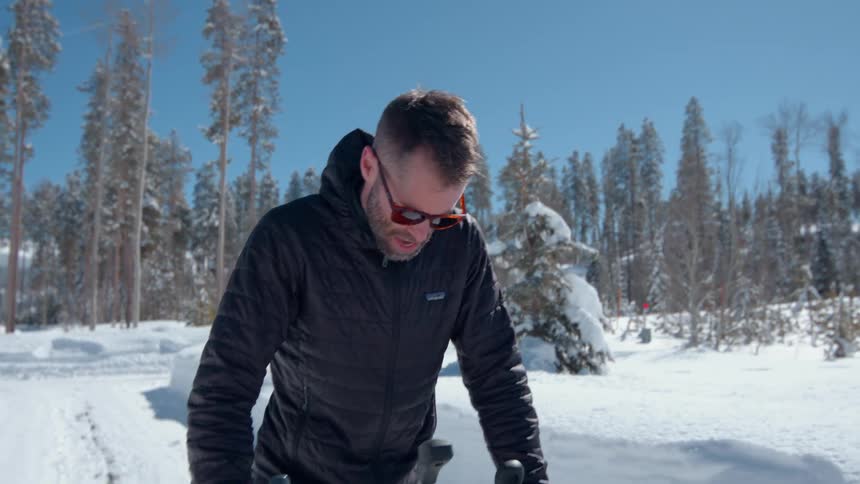 A man using a snow pusher on his driveway at midday wearing glasses and a winter jacket surrounded by snow