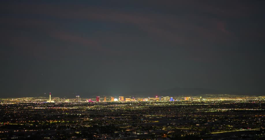 City skyline at night with a series of buildings silhouetted against the dark sky as orange clouds glow faintly across the horizon