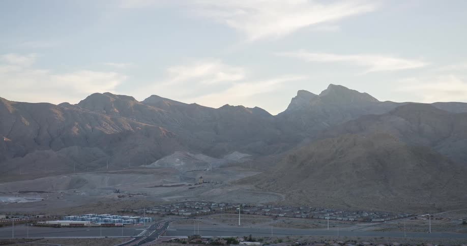 A sweeping panoramic view of a vast mountain range in a barren desertlike environment with a small town nestled at the base all under a hazy sky