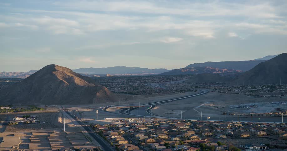A suburban desert town stretches toward winding highways and rocky mountains under soft morning light