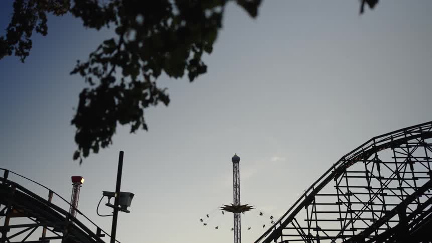 Roller coaster structure frames a swing ride against the evening sky