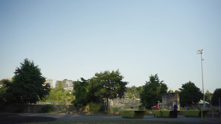 Two people playing ping pong on outdoor tables at a park in the morning