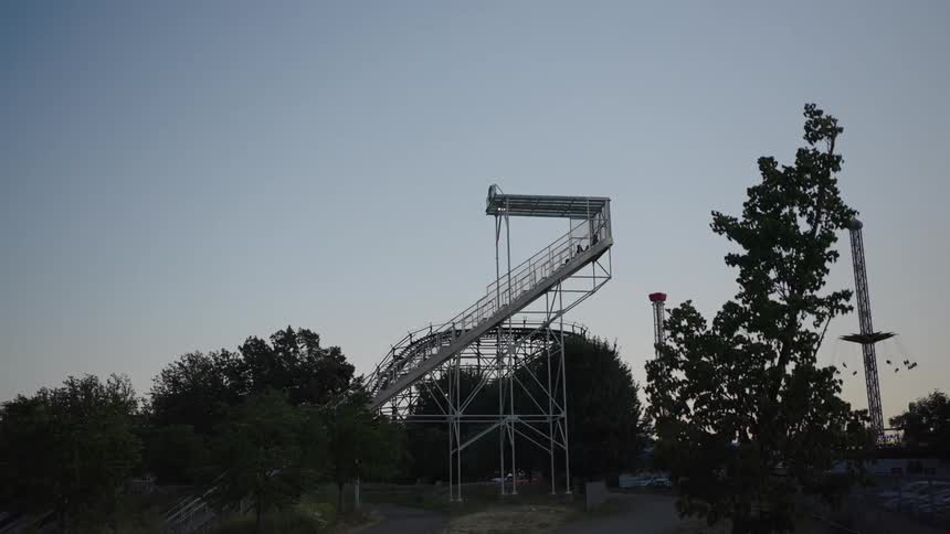 A tall roller coaster amusement park structure rises into the evening sky silhouetted against fading daylight
