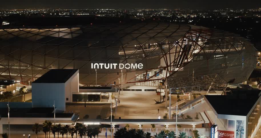 The intuit dome glows brightly at night in los angeles surrounded by palm trees and city lights