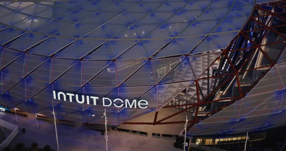 The intuit dome glows with blue lights at night showcasing its futuristic design and illuminated geometric structure