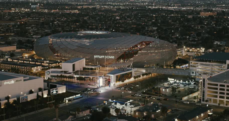 Intuit dome stadium lit up at dusk in the middle of the city