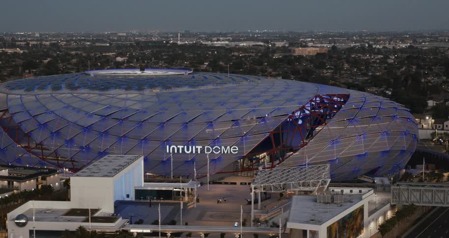 Dome stadium lit in blue stands out in the urban landscape at dusk