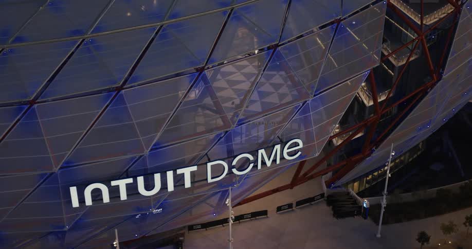 The intuit dome glows with blue lighting as evening falls over los angeles