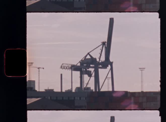 A silhouetted industrial crane looms over a port city under a soft lavender sky in the early morning