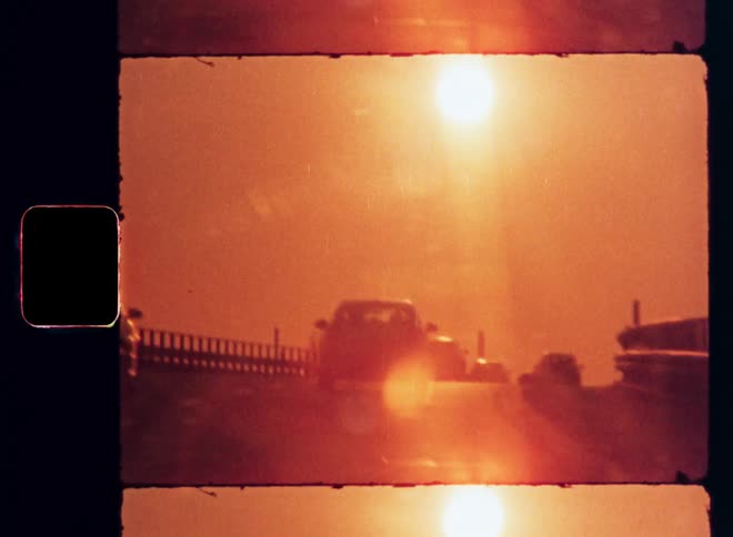 A car driving across a busy bridge as the orange setting sun casts a warm glow over the sky