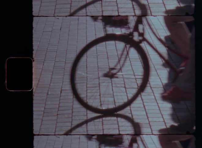 A bicycle and people move across brick pavement captured in a vintage film strip frame