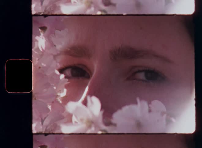 Portrait of beautiful brunette woman standing behind cherry blossoms slowly opening her brown eyes looking into the 8mm camera with a piercing glance and self-confidence and a seductive vibe