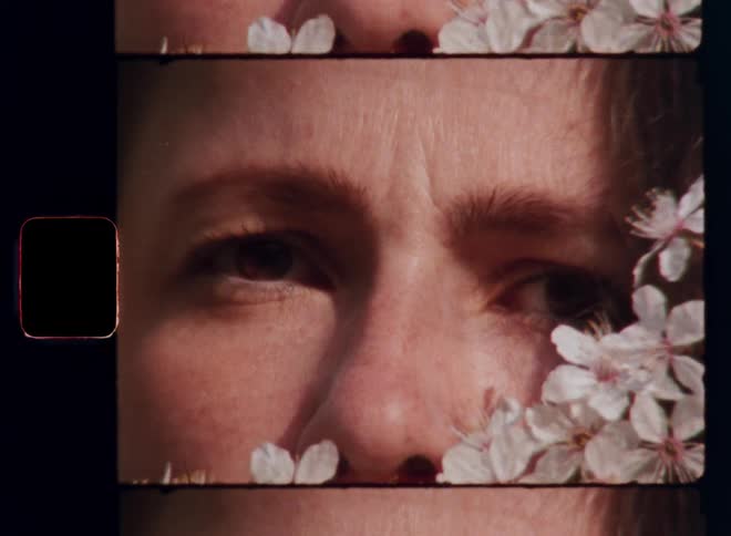 Vintage Super 8mm portrait close up of a woman’s eyes surrounded by white flowers closing and opening in slow motion while the warm sun shines into her face