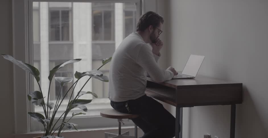 A man sits at a desk and works on a laptop