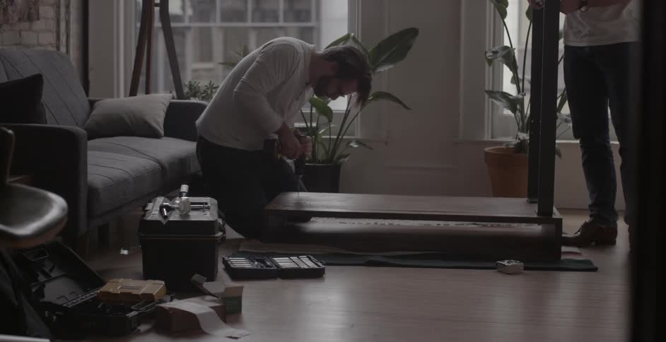 Two men assemble furniture on a living room floor