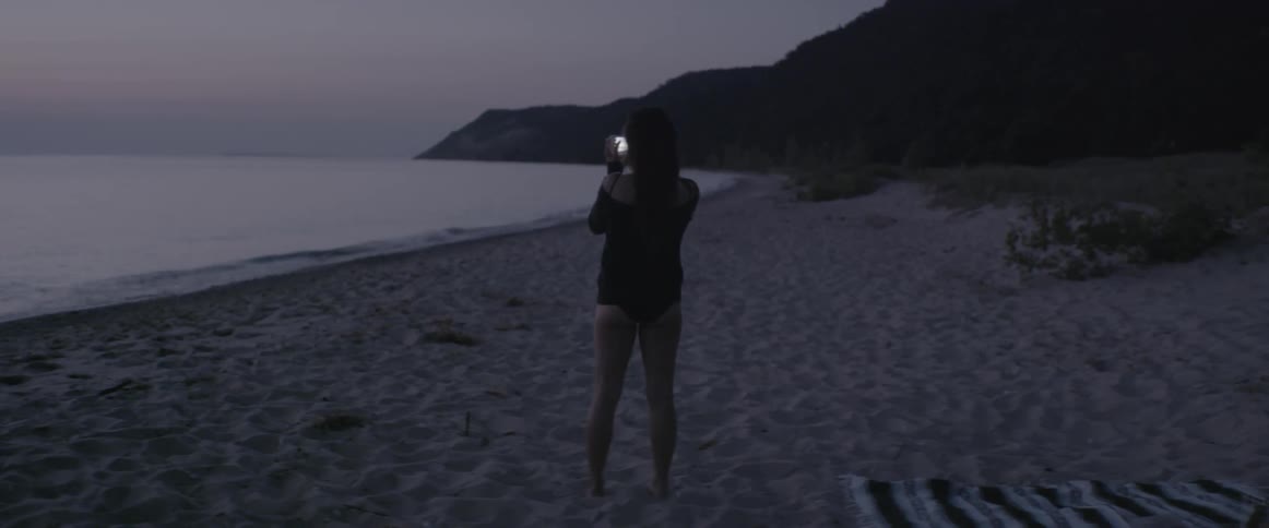 A woman takes a picture of the ocean at sunset
