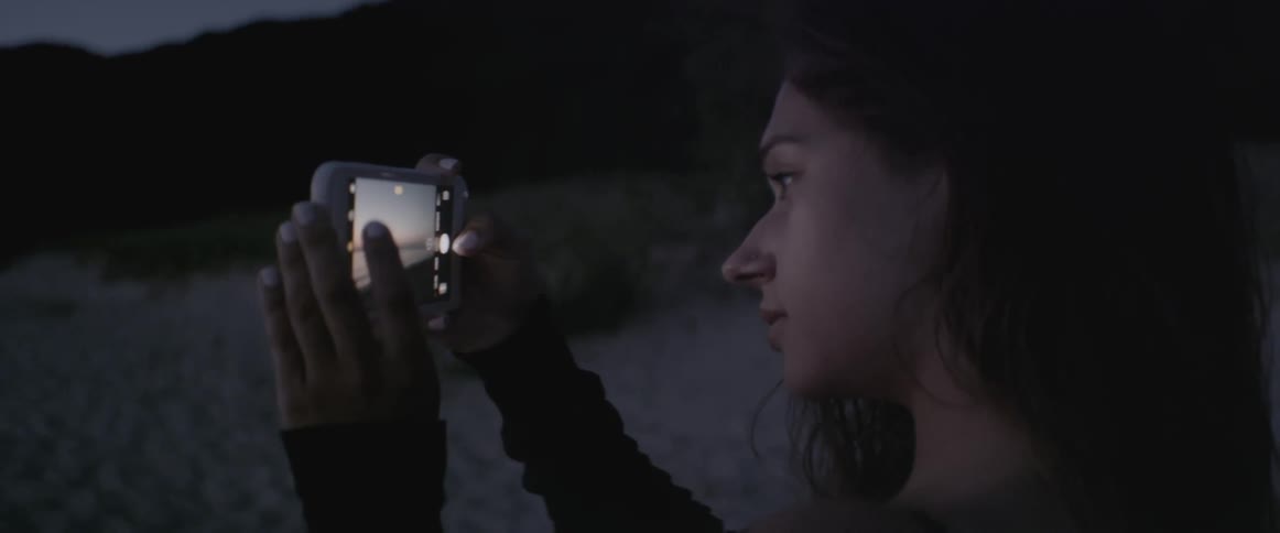 A woman takes a picture of the ocean at sunset