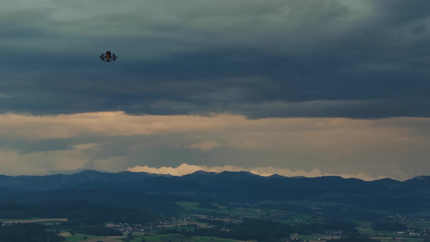 An FPV drone hovers over a vast mountainous landscape beneath dramatic stormy clouds