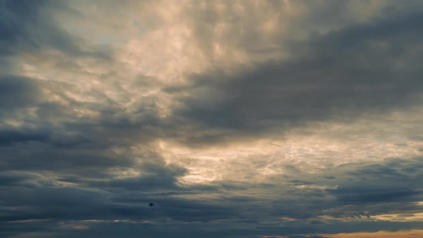 A drone flies under a cloudy sky
