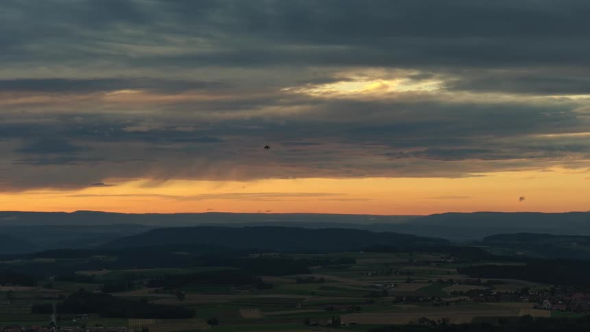 Drone flies over fields and hills toward the sunset