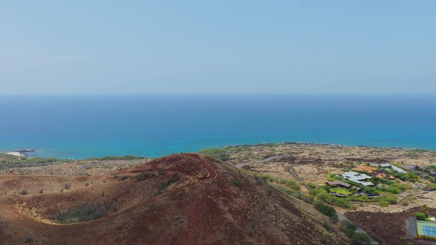 A coastal town with a hill on one side and a view of the ocean in the background at midday