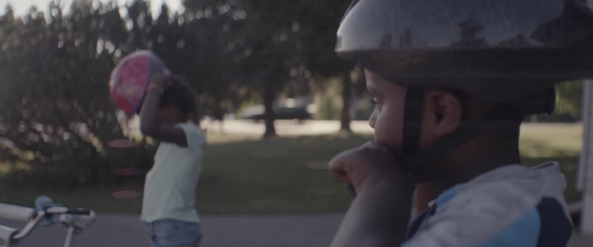 Young children put bicycle helmets on in a driveway