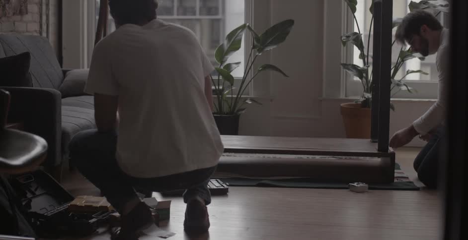 Two men putting together a piece of furniture in a house