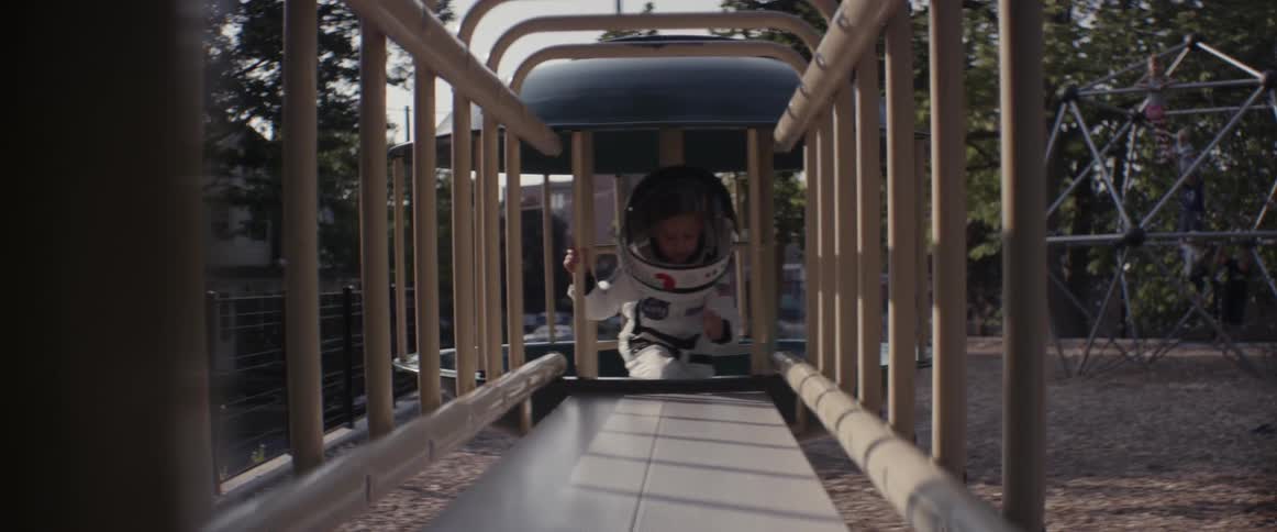 A girl in an astronaut costume climbs on a playground toy