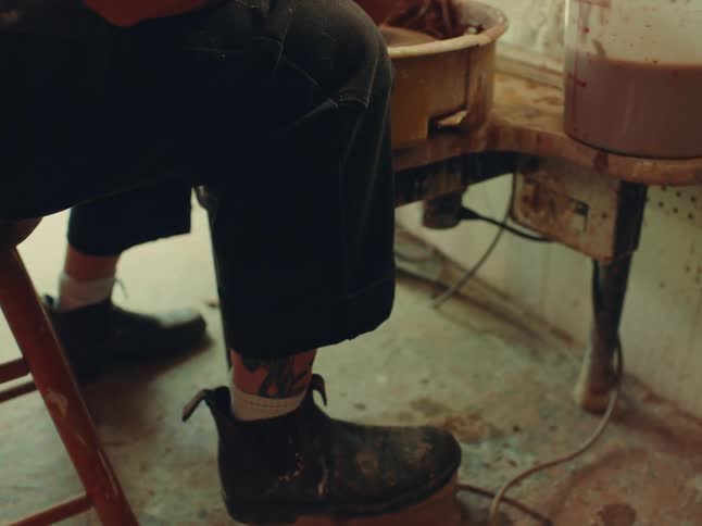 Tattooed person works on a pottery wheel shaping clay