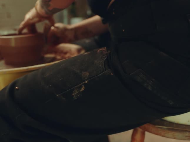 Hands shape clay around a pot on the pottery wheel