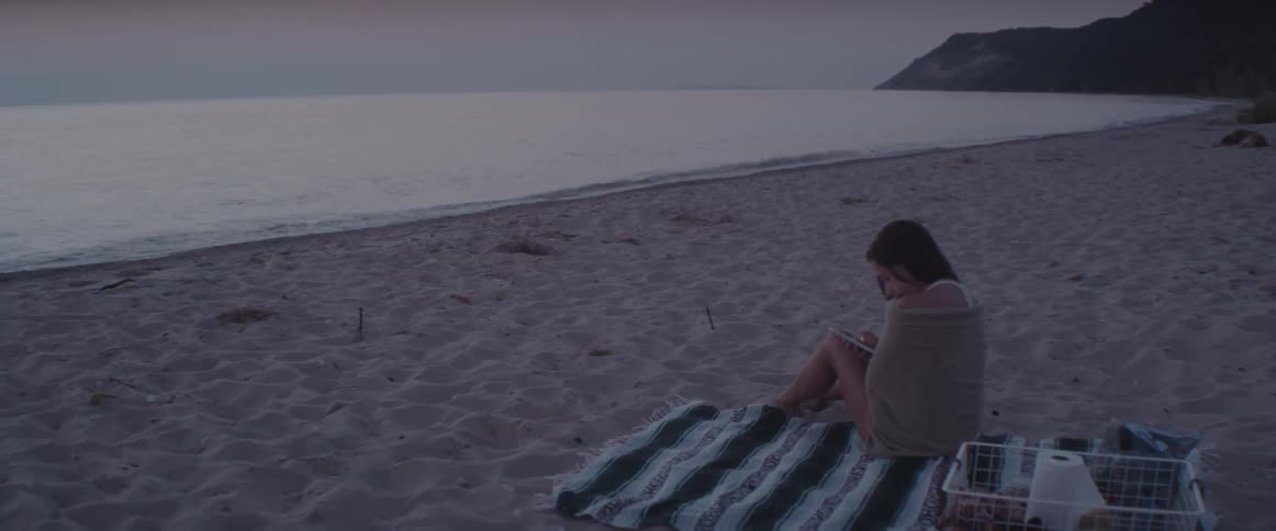 A woman sits on a beach at sunset