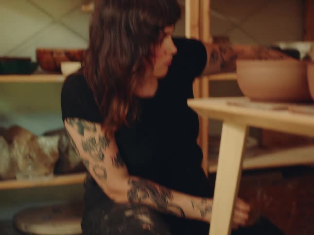 Tattooed woman in a black shirt arranges ceramic pieces on a shelf