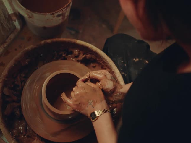 Pair of womans hands sculpting a vase with clay