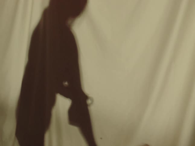 A womans reflection is seen through a cloth as she drops a pottery pot onto a table indoors