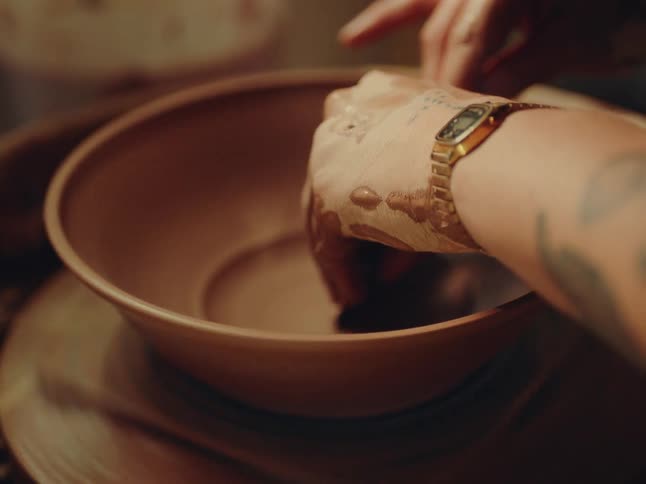 A person shapes clay on a pottery wheel