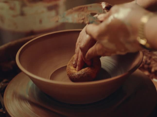 Hands skillfully shape a clay bowl on a pottery wheel indoors