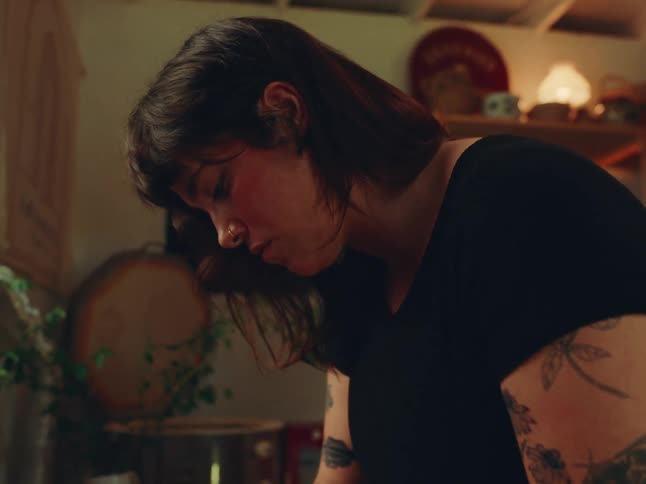 Brownhaired woman with tattoos on her arm works focused in a softly lit craft environment