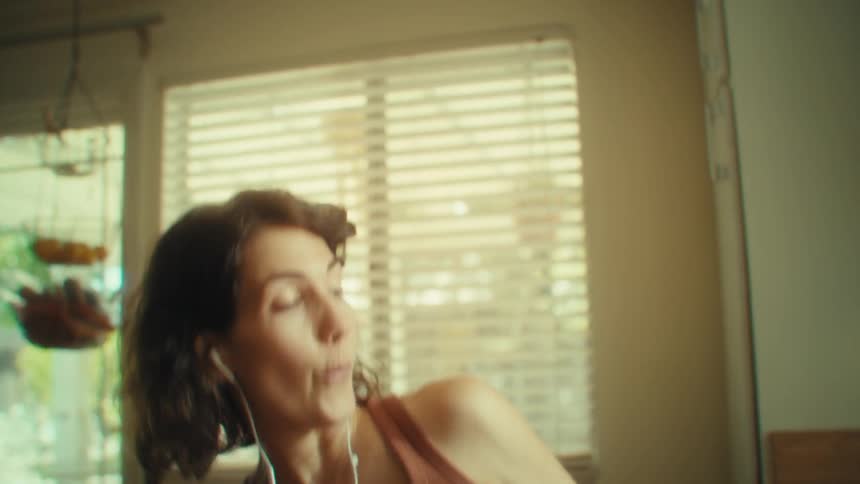 Woman with earphones sings and gestures cheerfully in the kitchen