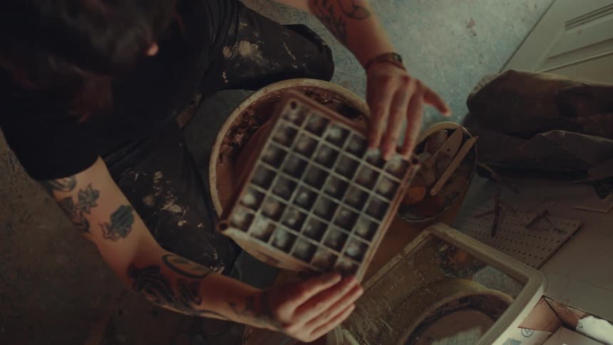 A woman makes a bowl and removes it from the pottery wheel to examine it before standing up from the chair she was sitting on