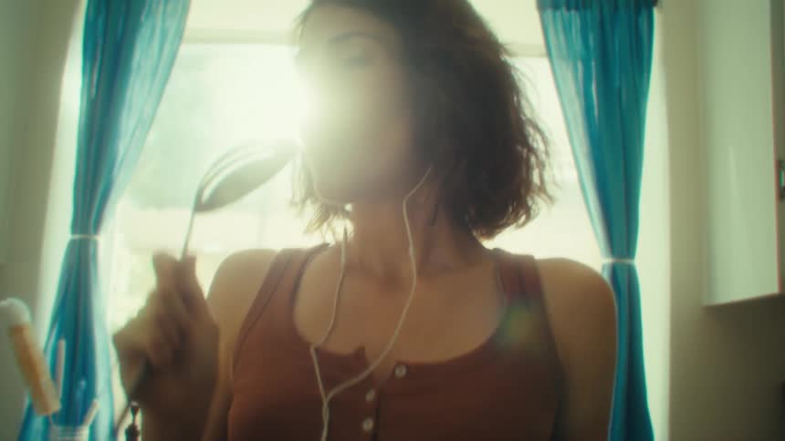 Woman sings in the kitchen holding a utensil as a microphone