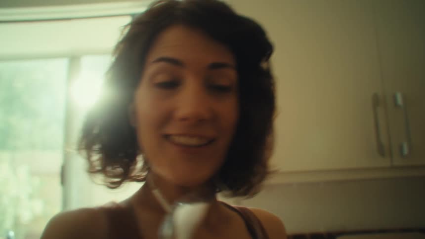 Woman enjoys singing in the kitchen with a metal spoon as a microphone