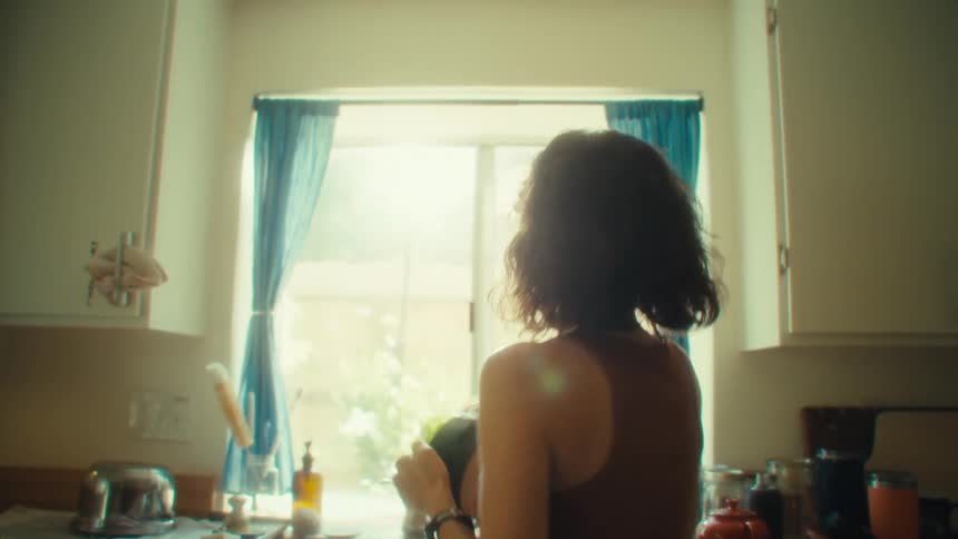 A young woman dancing excitedly in the kitchen while doing the dishes at midday wearing wired earbuds